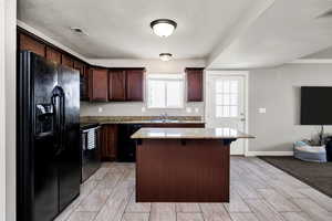 Kitchen with light stone counters, visible vents, a sink, a kitchen island, and black appliances