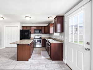 Kitchen featuring a kitchen breakfast bar, a sink, baseboards, a kitchen island, and black appliances