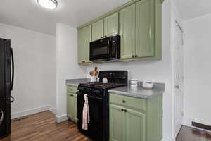 Kitchen with visible vents, baseboards, green cabinets, dark wood-type flooring, and black appliances