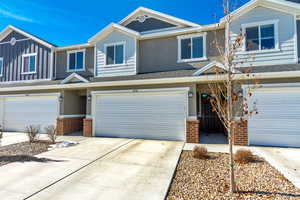 View of property with an attached garage, driveway, brick siding, and board and batten siding