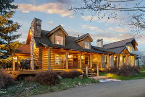 Log-style house with log exterior, a shingled roof, a chimney, and covered porch