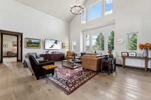 Living area featuring light wood-style floors, high vaulted ceiling, a notable chandelier, and a healthy amount of sunlight