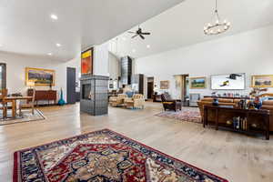 Living room with high vaulted ceiling, ceiling fan with notable chandelier, a glass covered fireplace, light wood-type flooring, and recessed lighting
