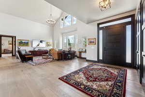 Foyer with high vaulted ceiling, an inviting chandelier, and light wood finished floors