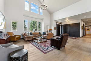 Living room featuring baseboards, recessed lighting, an inviting chandelier, light wood-style floors, and high vaulted ceiling