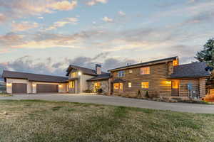 View of front facade featuring driveway, a chimney, log exterior, an attached garage, and a front yard