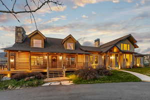 Log cabin with log exterior, roof with shingles, a chimney, and covered porch