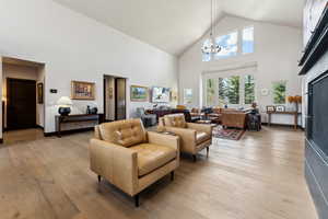 Living area with light wood-style floors, high vaulted ceiling, and an inviting chandelier