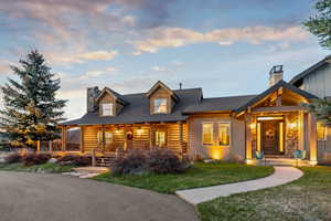 View of front of house with a chimney, a front lawn, roof with shingles, and covered porch