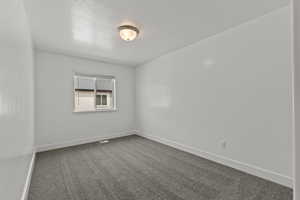 Empty room featuring dark colored carpet, a textured ceiling, and baseboards