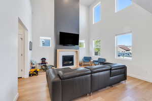 Living area featuring baseboards, light wood-style flooring, a towering ceiling, and a healthy amount of sunlight