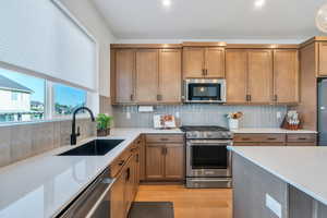 Kitchen with stainless steel appliances, a sink, light wood-type flooring, light stone countertops, and brown cabinetry