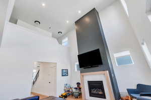 Living room featuring a fireplace, light  wood-style flooring, a high ceiling, and recessed lighting