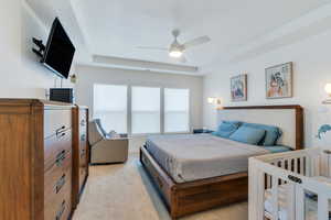 Bedroom with a raised ceiling, light colored carpet, and ceiling fan