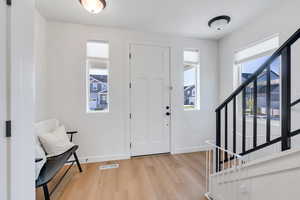 Foyer entrance with light  wood finished floors, visible vents, stairway, and a healthy amount of sunlight