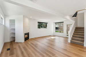 Unfurnished living room with a fireplace, stairway, visible vents, and light wood-type flooring
