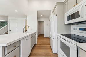 Kitchen featuring light wood finished floors, a sink, white appliances, and recessed lighting