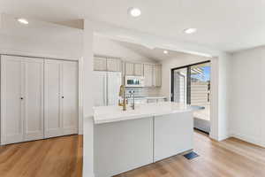 Kitchen featuring light countertops, white appliances, light wood-style floors, and vaulted ceiling