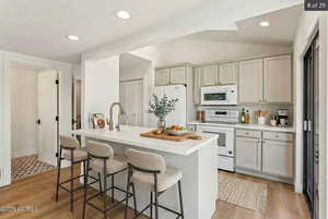Kitchen with light countertops, white appliances, lofted ceiling, a breakfast bar, and a center island with sink