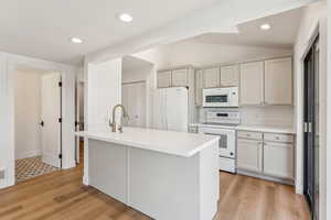 Kitchen with vaulted ceiling, a sink, white appliances, and light countertops