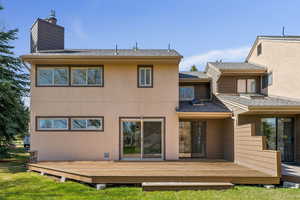Rear view of house featuring stucco siding, a chimney, and a deck