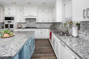 Kitchen with dark wood finished floors, blue cabinets, a sink, white oven, and white cabinetry