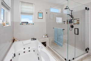 Primary bath featuring wainscoting, a tub with jets, a stall shower, and tile walls