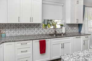 Kitchen featuring granite counters, decorative backsplash, white cabinetry, and a sink