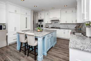 Kitchen with white cabinets, backsplash, stainless steel appliances, paneled fridge and a sink