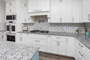 Kitchen with white double oven, white cabinetry, stainless steel gas cooktop, and tasteful backsplash