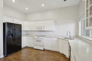 Kitchen featuring a sink, white appliances, white cabinetry, recessed lighting, and glass insert cabinets