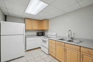 Kitchen with white appliances, light tile patterned floors, a paneled ceiling, and a sink