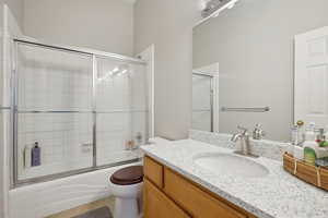 Full bathroom with vanity, bath / shower combo with glass door, and toilet