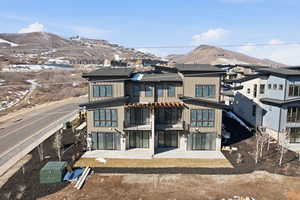 View of front facade with a patio, a mountain view, roof with shingles, and board and batten siding