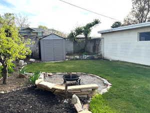 View of yard featuring fence, an outdoor fire pit, a storage unit, and fruit trees.