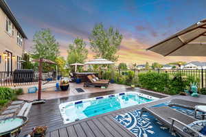 Pool at dusk with fence, hot tub deck surround, a deck, and area for grilling