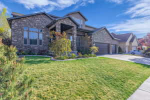 View of front facade featuring a front lawn, stone siding, and a garage