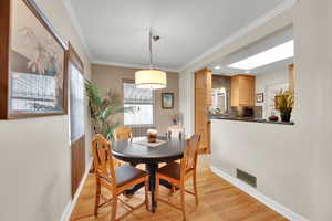 Dining space with ornamental molding, baseboards, a skylight, light wood finished floors, and visible vents