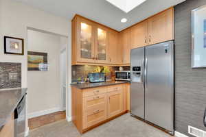 Kitchen featuring decorative backsplash, visible vents,stainless steel appliances, glass insert cabinets, and light brown cabinetry