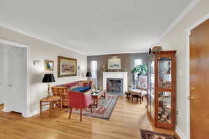 Living room featuring a fireplace with flush hearth, baseboards, crown molding, and light wood finished floors