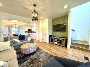 Living area with an inviting chandelier, a tray ceiling, light wood-style flooring, baseboards, and recessed lighting