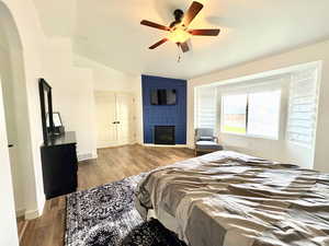Bedroom with lofted ceiling, wood finished floors, visible vents, a large fireplace, and ceiling fan