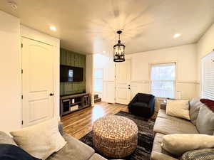 Living room with a decorative wall, wood finished floors, a chandelier, a wainscoted wall, and recessed lighting