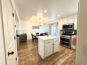 Kitchen featuring wood finished floors, a chandelier, stainless steel appliances, a tray ceiling, and white cabinetry