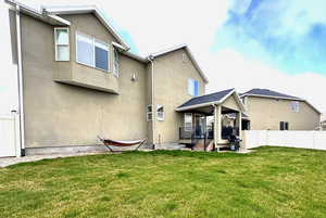 Rear view of house featuring stucco siding, a lawn, and fence