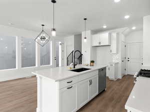 Kitchen with a sink, light wood-style floors, hanging light fixtures, appliances with stainless steel finishes, and white cabinetry