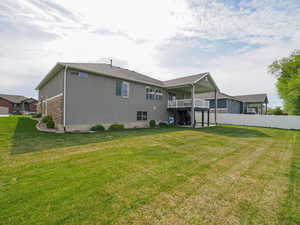 Rear view of house with stucco siding, a lawn, and fence