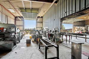 Interior space featuring a towering ceiling, concrete floors, a workshop area, and metal wall