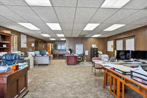Office area featuring a paneled ceiling, carpet flooring, and wood walls