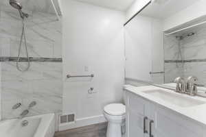 Bathroom with wood finished floors, vanity,  shower combination, toilet, and visible vents
